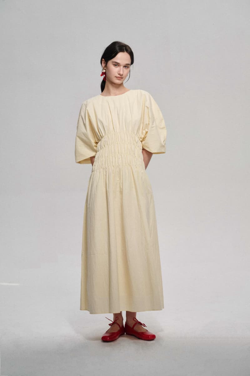 A woman wearing a long beige dress with a pleated waist and puff sleeves.